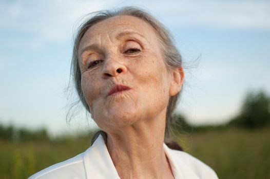 Portrait of senior woman with grey hair and face with wrinkles wearing white jacket and relaxing at park during sunny day, happy retirement, mothers day concepts