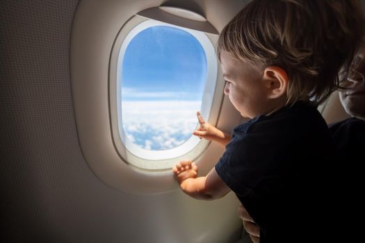 cute toddler points his finger at the sky through the window. first flight concept, traveling with children