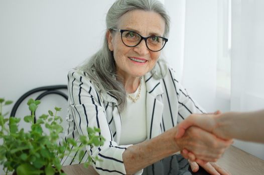 Mature businesswoman is leading an interview with new colleague and shaking their hand at the end. Business people concept.