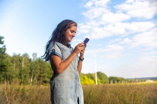 happy young woman looks into smartphone on nature background on sunny day