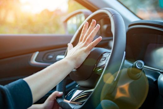 female hand presses the horn on the steering wheel of a modern car. no face