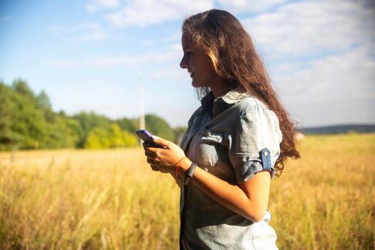 happy young woman looks into smartphone on nature background on sunny day