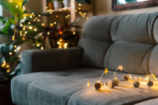 Christmas natural eco decoration, pine cone, lights on gray couch background at cozy home. Glowing light bokeh, coniferous branch. Winter holidays. Zero waste, plastic free. Indoors plants