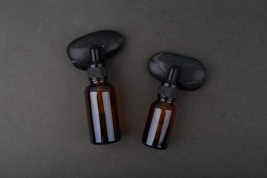 Flat lay in dark tones with two glass serum bottles with dropper on black background. Concept of skin care beauty products for man