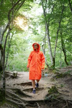 Young woman in orange raincoat hiking in green forest. Active lifestyle and travel