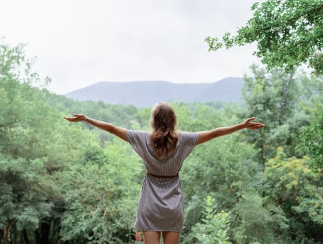 Travel and freedom concept. Back view of a young woman in summer dress standing on a big rock in the forest looking away