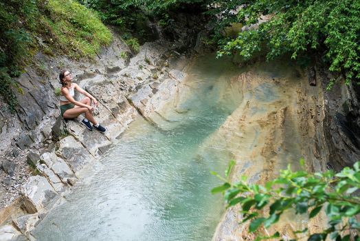 Summer travel travel. Hiking. Young happy woman enjoing the nature, sitting by the mountain river.