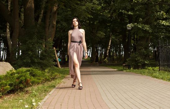 young beautiful brunette woman in beige dress walking on the sidewalk in summer