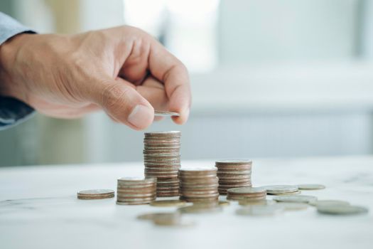 Businessman saving money concept. Hand holding coins putting in jug glass