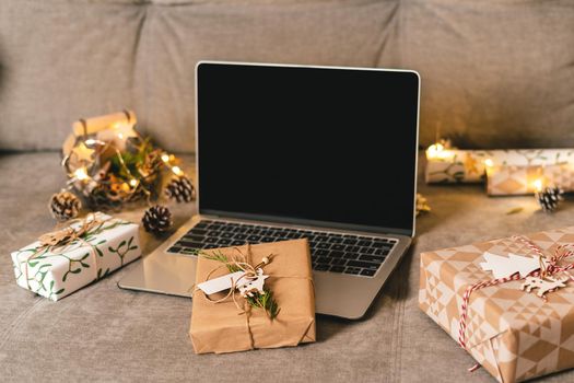 Online shopping at Christmas holidays. Gifts, and mock up screen laptop on couch with natural eco presents and decor. Merry Christmas. Wrapping present boxes