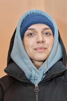 Facial portrait of a pretty girl in a hat and dark jacket with a hood looking at the camera