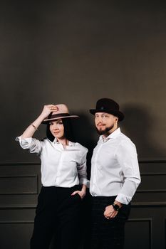 A man and a woman in white shirts and hats on a black background.A couple in love poses in the interior of the studio.