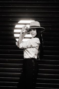 Elegant brunette girl in a white shirt and beige hat on a dark background. black and white photo.