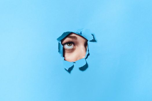 woman peeping through the holes in the poster blue studio background. High quality photo