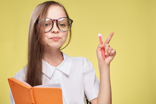 schoolgirl with textbook in hands learning childhood yellow background. High quality photo