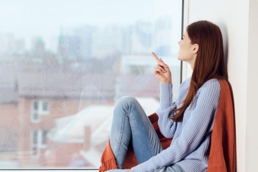 woman with sad expression sits by the window with a plaid. High quality photo