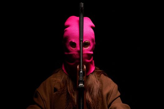 woman in a pink mask the gun crime Gangster danger the dark background. High quality photo