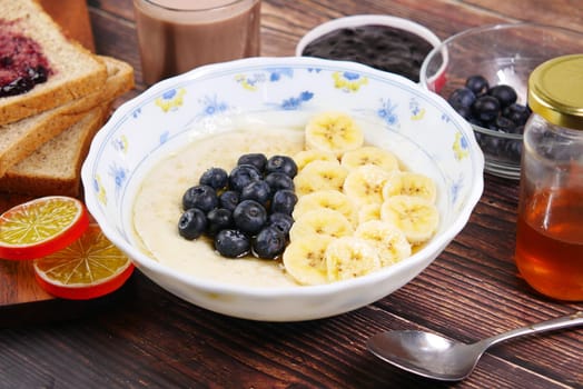 a bowl of oats, berry, banana and honey on table .