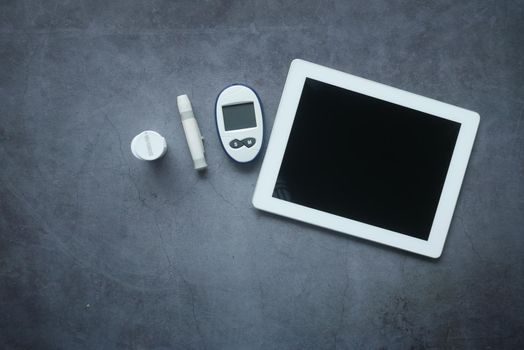 top view of digital tablet, pills and diabetic measurement tool on table.