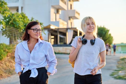 Summer walk of smiling mom and teenage daughter. Time together, family, communication parent-child adolescent, vacation, weekend, mother and daughter teenager concept