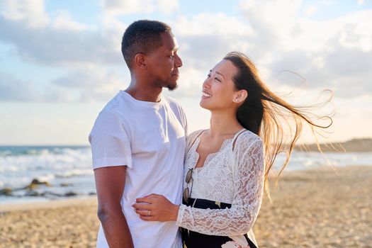 Portrait of happy young beautiful couple on beach. Interracial couple, african american man and asian woman embracing at seaside. People, relationships, dating, vacation, tourism, multi-ethnic family