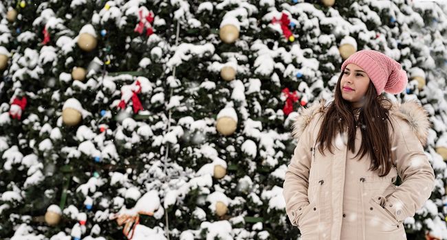Merry Christmas and happy New Year. Banner. Christmas background. Happy Woman in warm winter clothes standing by the big christmas tree outdoors, snow falling