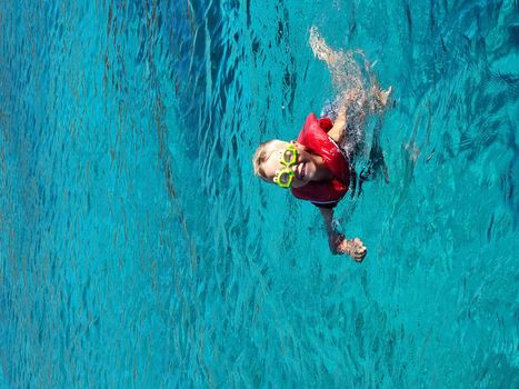 A child in swimming goggles and jelly bathes in the sea. Blue clear water.