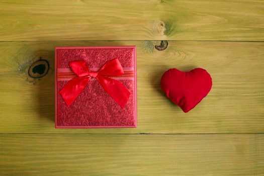 Gift in beautiful red box and heart on wooden table.