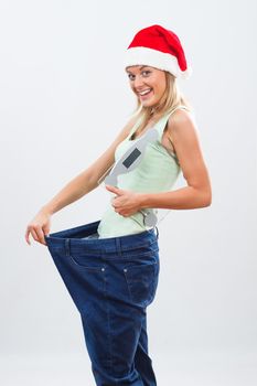 Happy woman with Santa hat in oversize jeans holding weight scale.