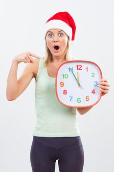 Portrait of woman with Santa hat in panic  pointing at clock.