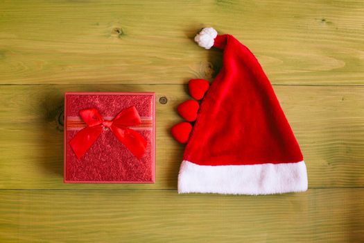 Image of Santa Hat and gift and heart shapes on wooden table.