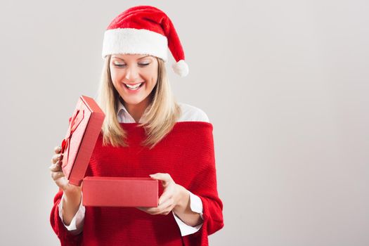 Happy young woman with Santa hat opening Christmas gift.