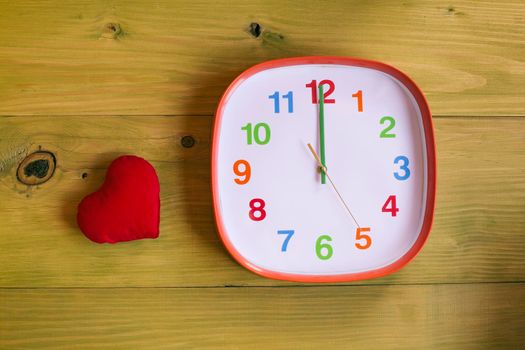 Image of clock showing midnight and heart on wooden table.