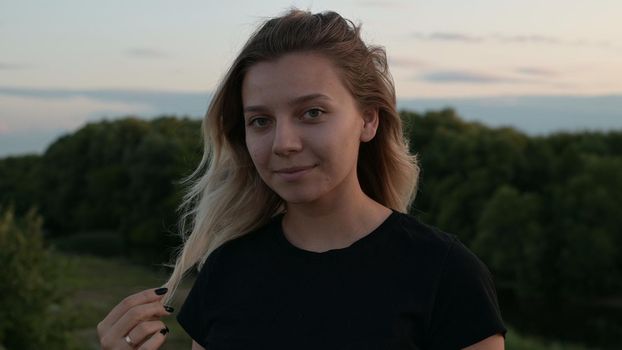 portrait of a beautiful smiling blonde girl standing in the wind against the background of autumn nature at sunset concept of emotions.