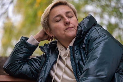 a girl in a dark jacket is sitting on a bench against the background of autumn nature, thinking and looking ahead.