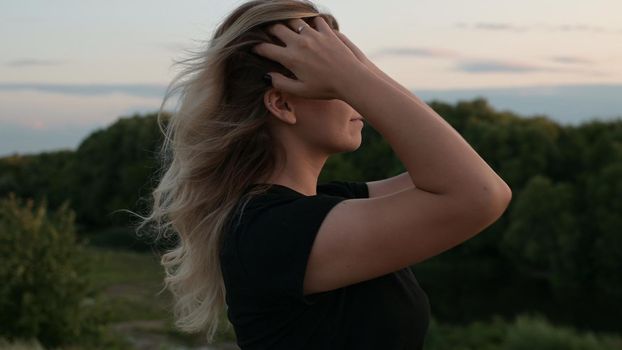 portrait of a beautiful long-haired smiling blonde girl standing in the wind against the background of autumn nature at sunset concept of emotions.