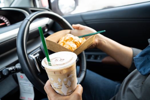 Asian lady holding ice coffee and bread bakery in car dangerous and risk an accident.