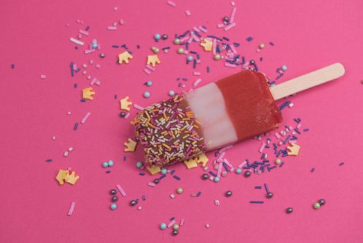 Ice cream on stick with colorful sprinkles over pink background