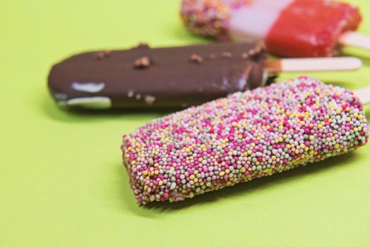 Set of ice cream on stick with colorful sprinkles over green background