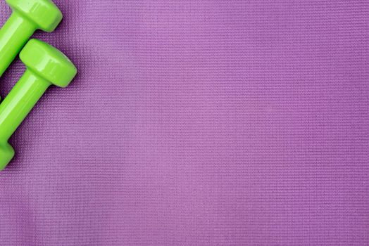 Ladie's dumbbells over purple fitness mat, top view. Sport concept
