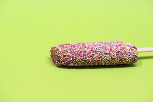 Ice cream on stick with colorful sprinkles over green background