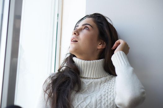 pretty woman in white sweater near the window. High quality photo