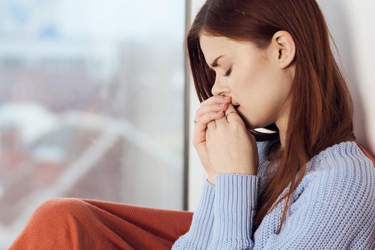 woman with sad expression sits by the window with a plaid. High quality photo