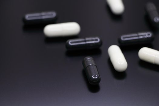 Black and white gel pill capsules abstract on smooth black surface