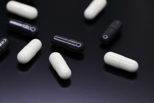 White and black gel pill capsules abstract on smooth black surface