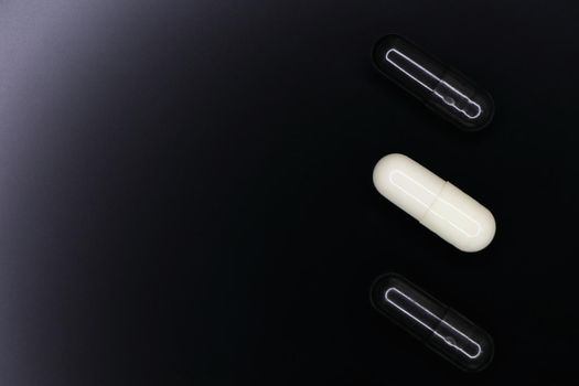 Black and white gel pill capsules layout on smooth black background