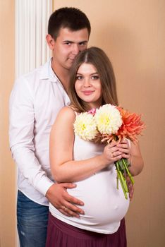 Happy Young pregnant woman and her husband with a bouquet of flowers at home