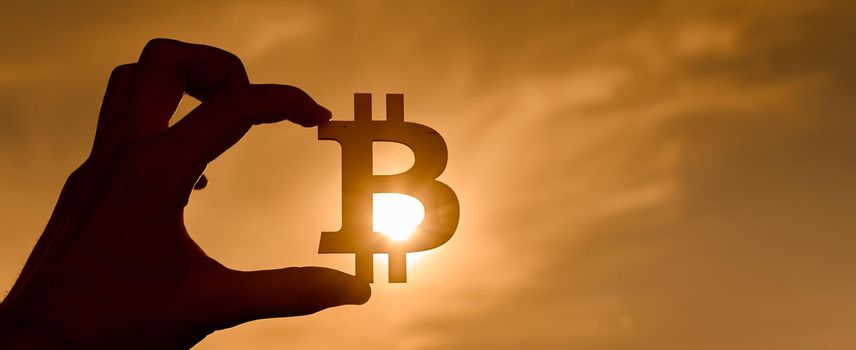 Bitcoin symbol in hand at sunset. sun through the sign. High quality photo