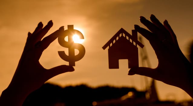 symbol of the dollar and the house at sunset in the form of contours in women's hands. High quality photo
