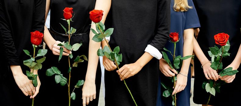 five girls in dark dresses hold one rose flower. High quality photo